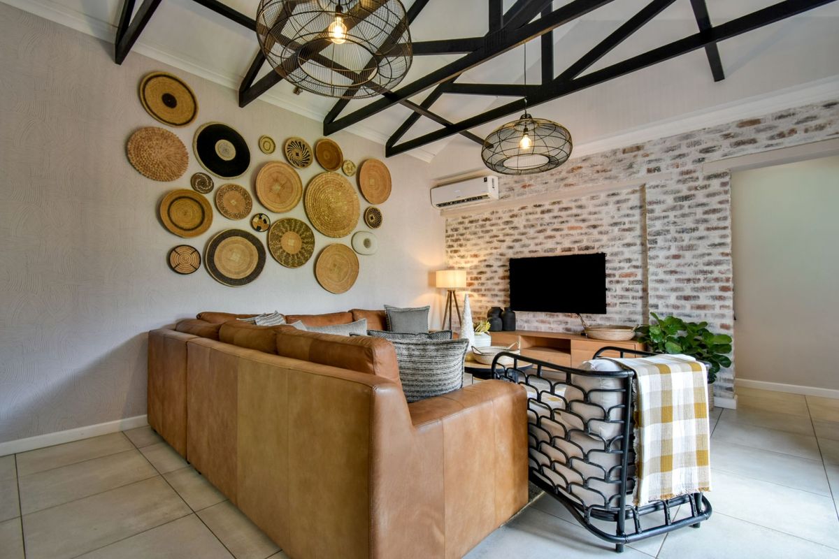 A well-appointed living room featuring exposed timber roof trusses, an exposed brick feature wall, and modern split-system air conditioning.
