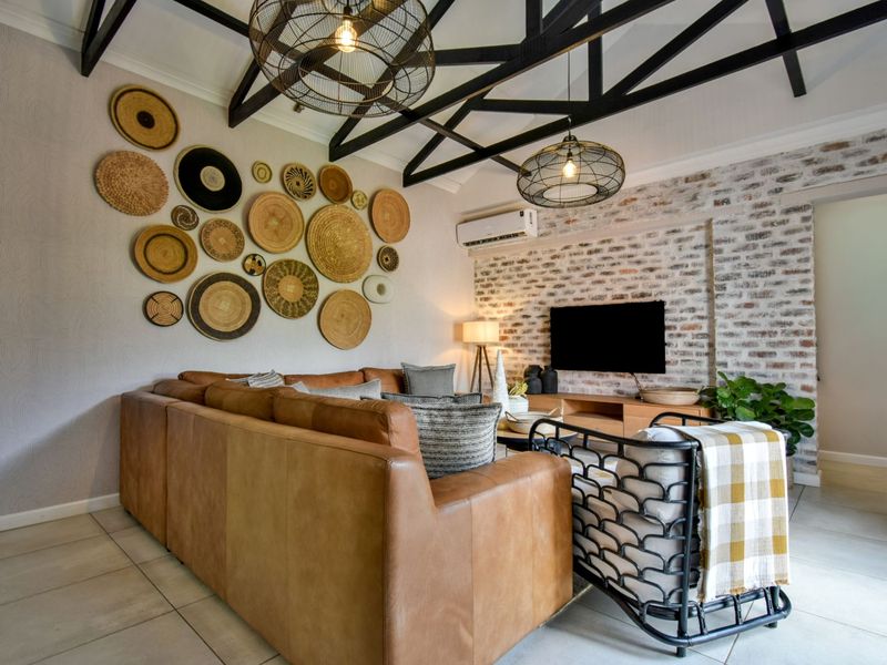 A well-appointed living room featuring exposed timber roof trusses, an exposed brick feature wall, and modern split-system air conditioning.