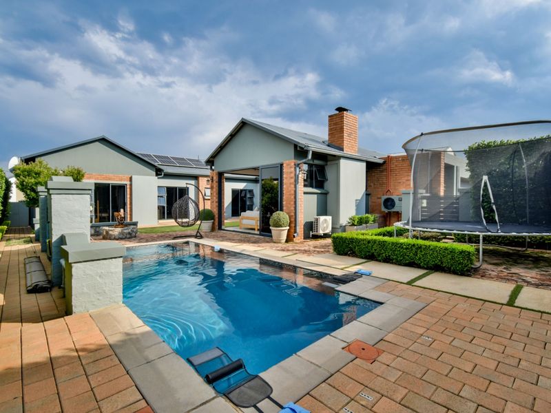 A well-maintained rear garden area featuring a swimming pool, brick paving, and modern home exterior with sliding glass doors and solar panels.