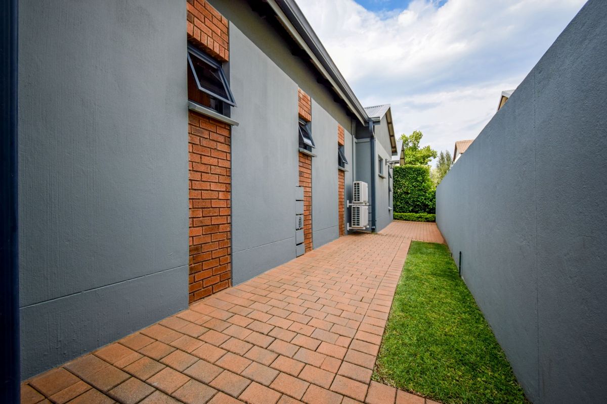 A well-maintained side passage featuring neat brick paving, a manicured lawn strip, and modern grey exterior walls with brick detailing.