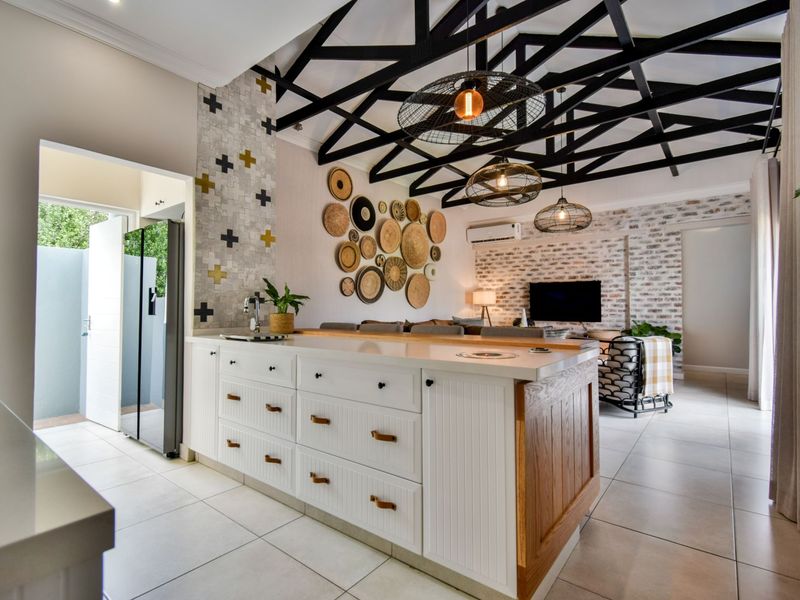 Modern open-plan living area featuring a large kitchen island, exposed black roof trusses, and a stylish feature brick wall.