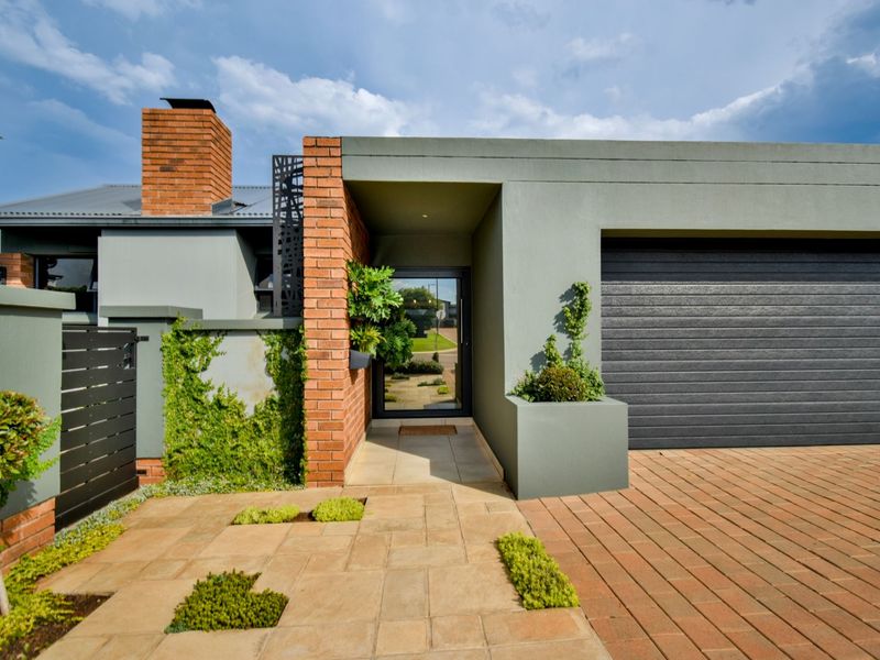 Modern front facade featuring a brick chimney, paved driveway, integrated garage, and a welcoming covered entrance with contemporary architectural finishes.