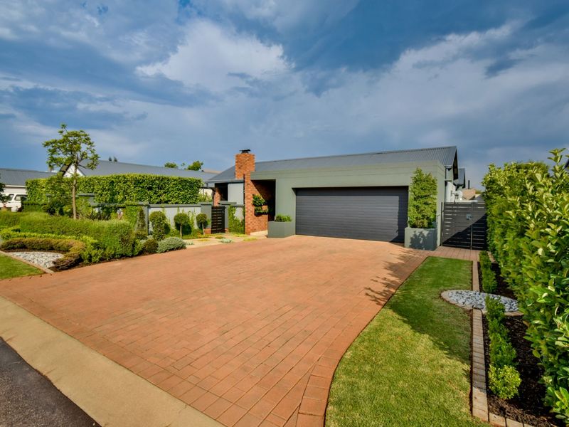 Front elevation of a modern home featuring a brick driveway, double garage, and well-maintained landscaped garden.