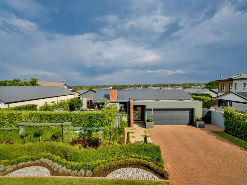 Elevated view of the front facade featuring a double garage, brick paved driveway, and well-maintained landscaped garden with mature hedging.