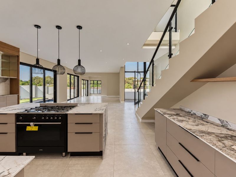 Spacious open-plan kitchen and living area featuring a modern island with gas cooktop, stone countertops, and a sleek staircase with glass balustrade.
