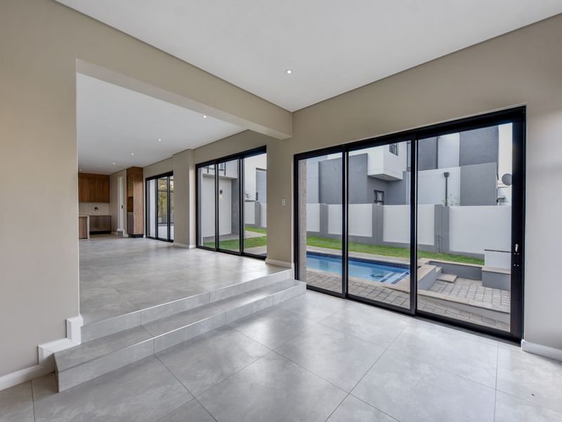 Spacious open-plan living area featuring large sliding glass doors, modern tiled flooring, and seamless flow to the outdoor pool and garden area.