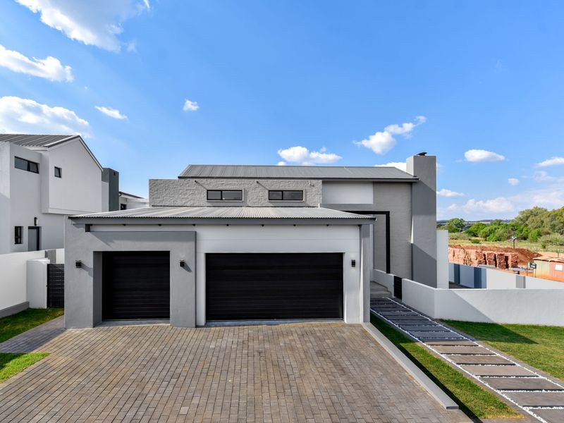 Modern double-story residential home featuring a double garage, paved driveway, and contemporary architectural finishes with stone cladding and a metal roof.