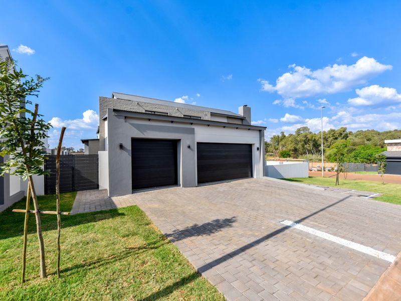 Modern residential exterior featuring a double garage with dark metal doors and a spacious paved driveway, set within a well-maintained landscaped property.