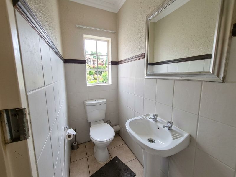 A functional guest bathroom featuring a pedestal basin, toilet, and half-tiled walls with a window providing natural light.