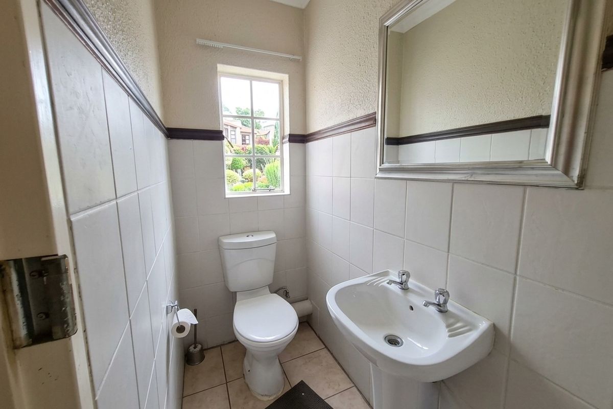 A functional guest bathroom featuring a pedestal basin, toilet, and half-tiled walls with a window providing natural light.