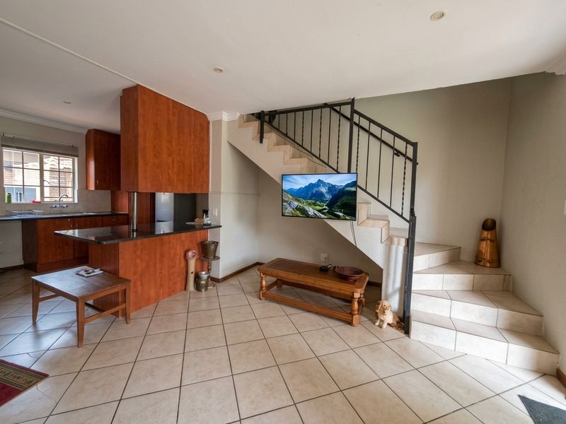 Open plan living area featuring tiled floors, a staircase with metal railing, and a kitchen with wood-finish cabinetry and granite countertops.