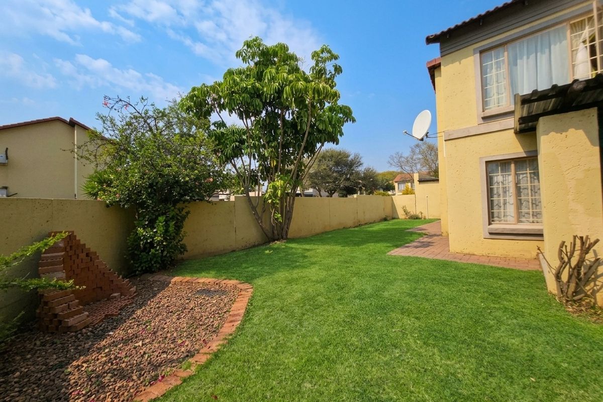 A private rear garden featuring a well-maintained lawn, paved pathway, and perimeter boundary wall, providing a secure outdoor space for the townhouse.