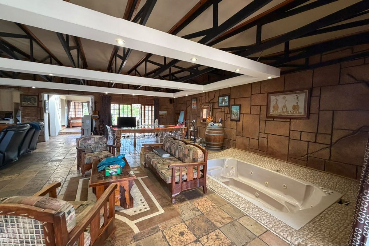 Spacious living area featuring exposed steel roof trusses, a stone-clad feature wall, and a built-in jetted bathtub integrated into the tiled floor.