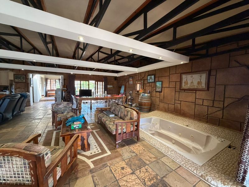 Spacious living area featuring exposed steel roof trusses, a stone-clad feature wall, and a built-in jetted bathtub integrated into the tiled floor.