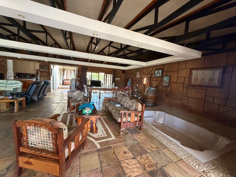 Spacious open-plan living area featuring exposed steel roof trusses, stone-clad walls, tiled flooring, and a unique integrated indoor spa bath.