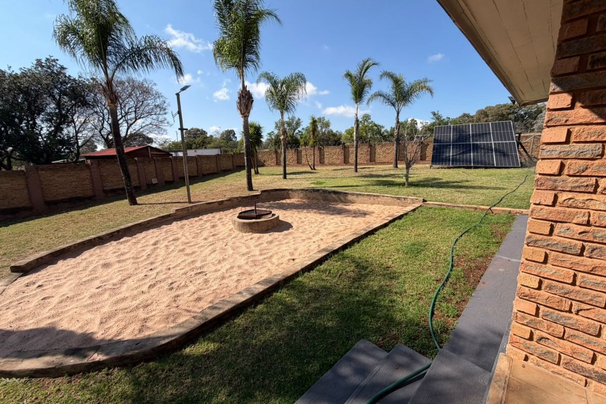 Spacious rear garden featuring a brick boundary wall, a sand pit with a fire pit, and a ground-mounted solar panel array.