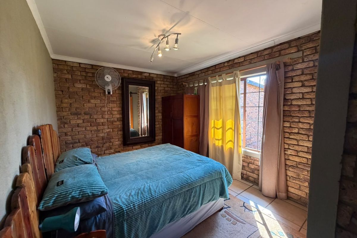 A bedroom featuring exposed brick walls, tiled flooring, and a wall-mounted fan, offering a rustic aesthetic with potential for modern updates.