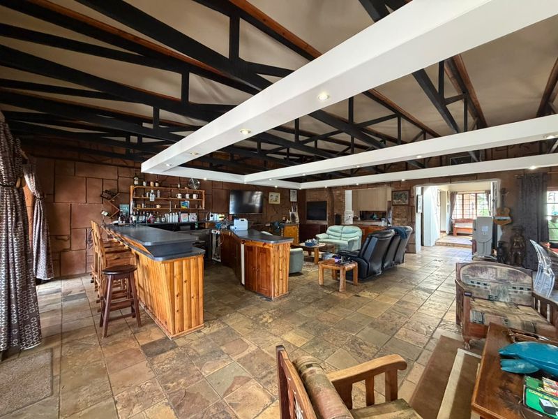 Spacious open-plan living area featuring exposed timber roof trusses, stone tile flooring, and a large built-in wooden bar counter with stone wall accents.
