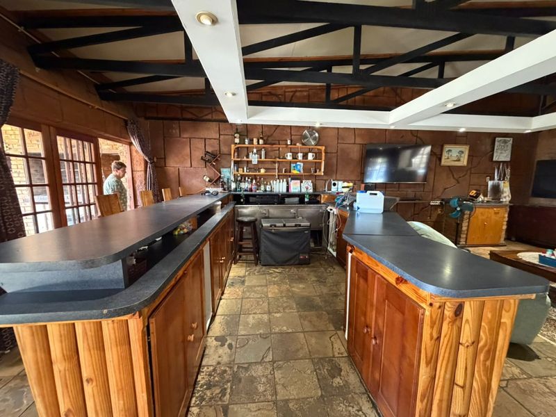 A rustic bar area featuring a large built-in counter, stone tile flooring, and exposed timber roof trusses, offering a classic entertainment space.