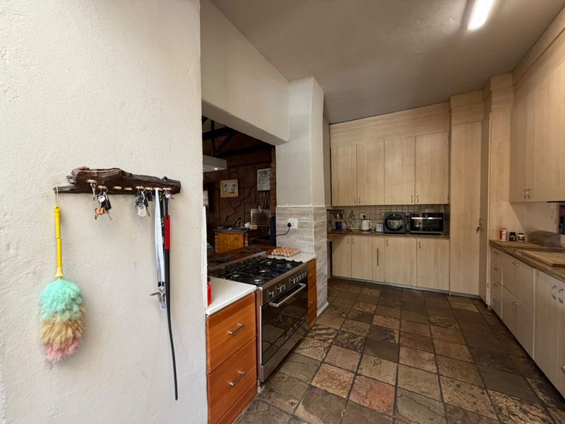A functional kitchen featuring light wood cabinetry, a gas stove with oven, and durable stone tile flooring, with an open flow to the adjacent living area.