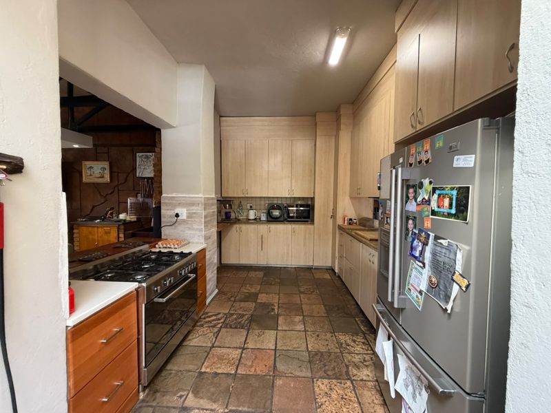 A functional kitchen featuring light wood cabinetry, stone tile flooring, and a built-in gas stove, with an open-plan layout connecting to an adjacent living area.
