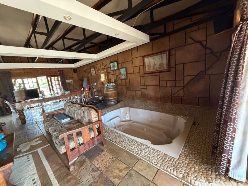 Spacious open-plan living area featuring a unique sunken jetted bathtub, exposed roof trusses, and rustic stone wall finishes.