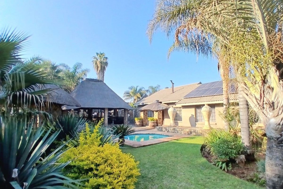 Rear view of the property featuring a swimming pool, a traditional thatched lapa, and solar panels installed on the main roof.