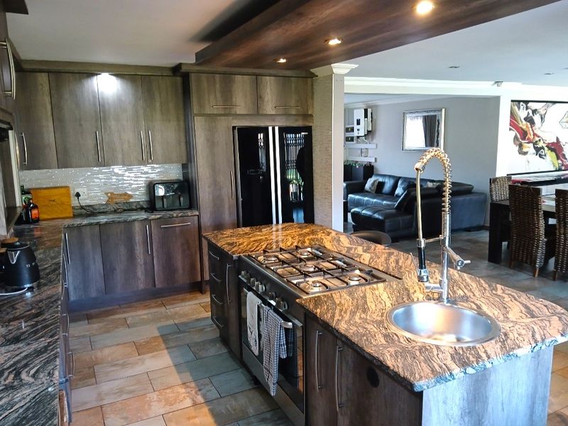 Modern open-plan kitchen featuring granite countertops, a central island with a gas hob and sink, and dark wood cabinetry, flowing into the living area.
