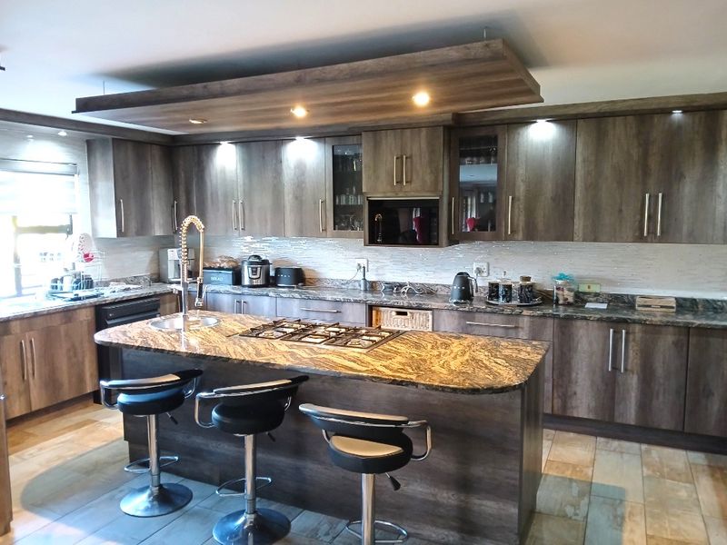 Modern kitchen featuring dark wood cabinetry, granite countertops, a central island with a gas hob, and integrated lighting features.