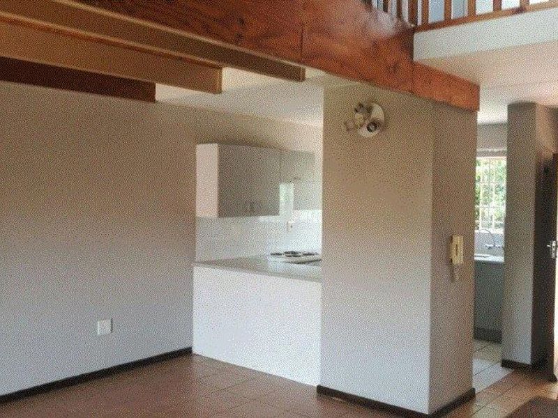 Open plan living area featuring exposed timber beams, tiled flooring, and a functional kitchen space with built-in cabinetry and hob.