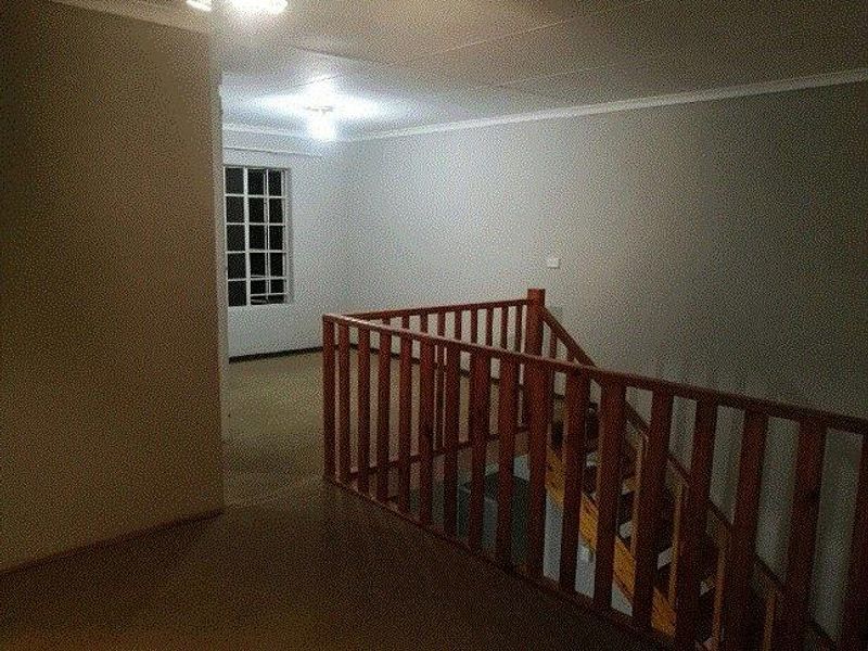 An empty upper-level landing area featuring a wooden balustrade overlooking the staircase, with neutral walls and a multi-pane window.