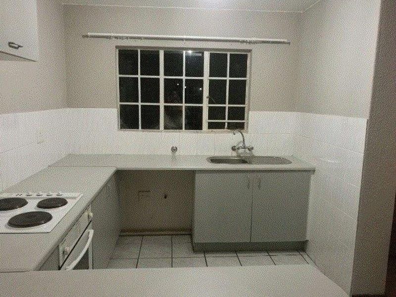 A functional kitchen featuring built-in cabinetry, laminate countertops, a stainless steel sink, and an integrated electric hob and oven with tiled splashbacks.