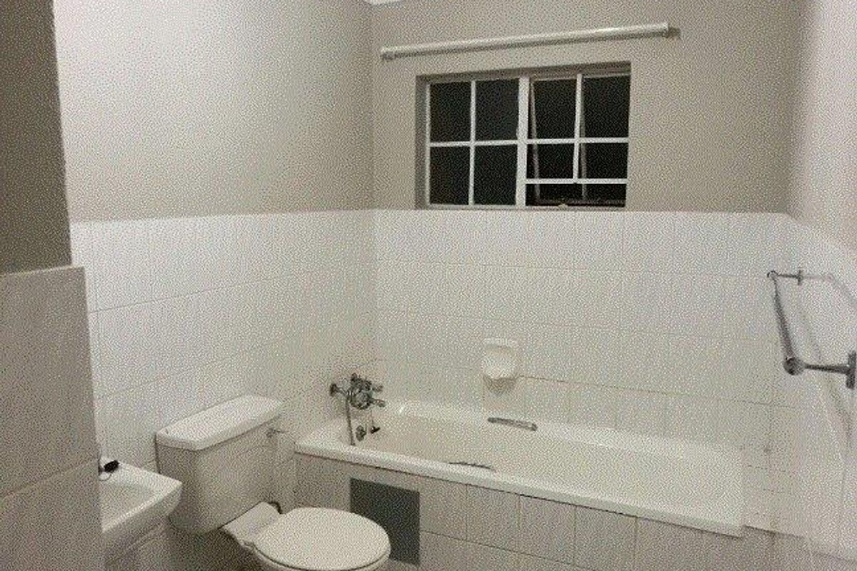 A functional bathroom featuring a bathtub, toilet, and basin with neutral wall tiling and a window for natural light.