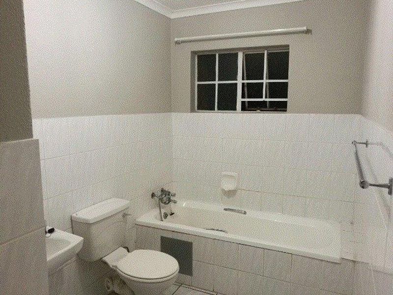 A functional bathroom featuring a bathtub, toilet, and basin with neutral wall tiling and a window for natural light.