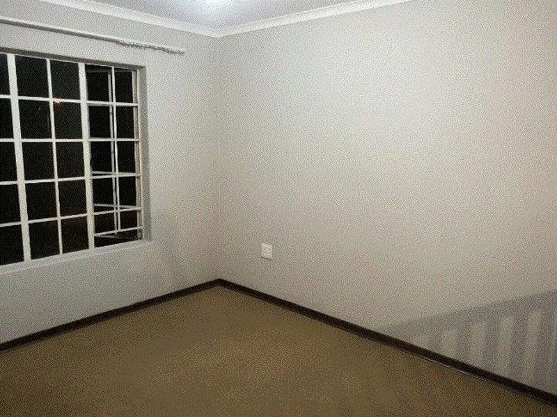 An empty bedroom featuring neutral walls, carpeted flooring, and a window fitted with security burglar bars.