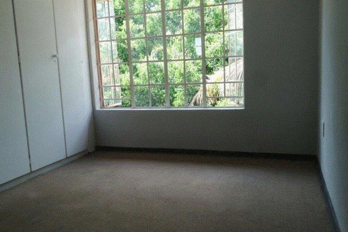 An empty bedroom featuring built-in cupboards, carpeted flooring, and a large window providing natural light and a view of the surrounding greenery.
