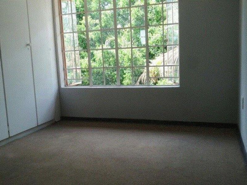 An empty bedroom featuring built-in cupboards, carpeted flooring, and a large window providing natural light and a view of the surrounding greenery.