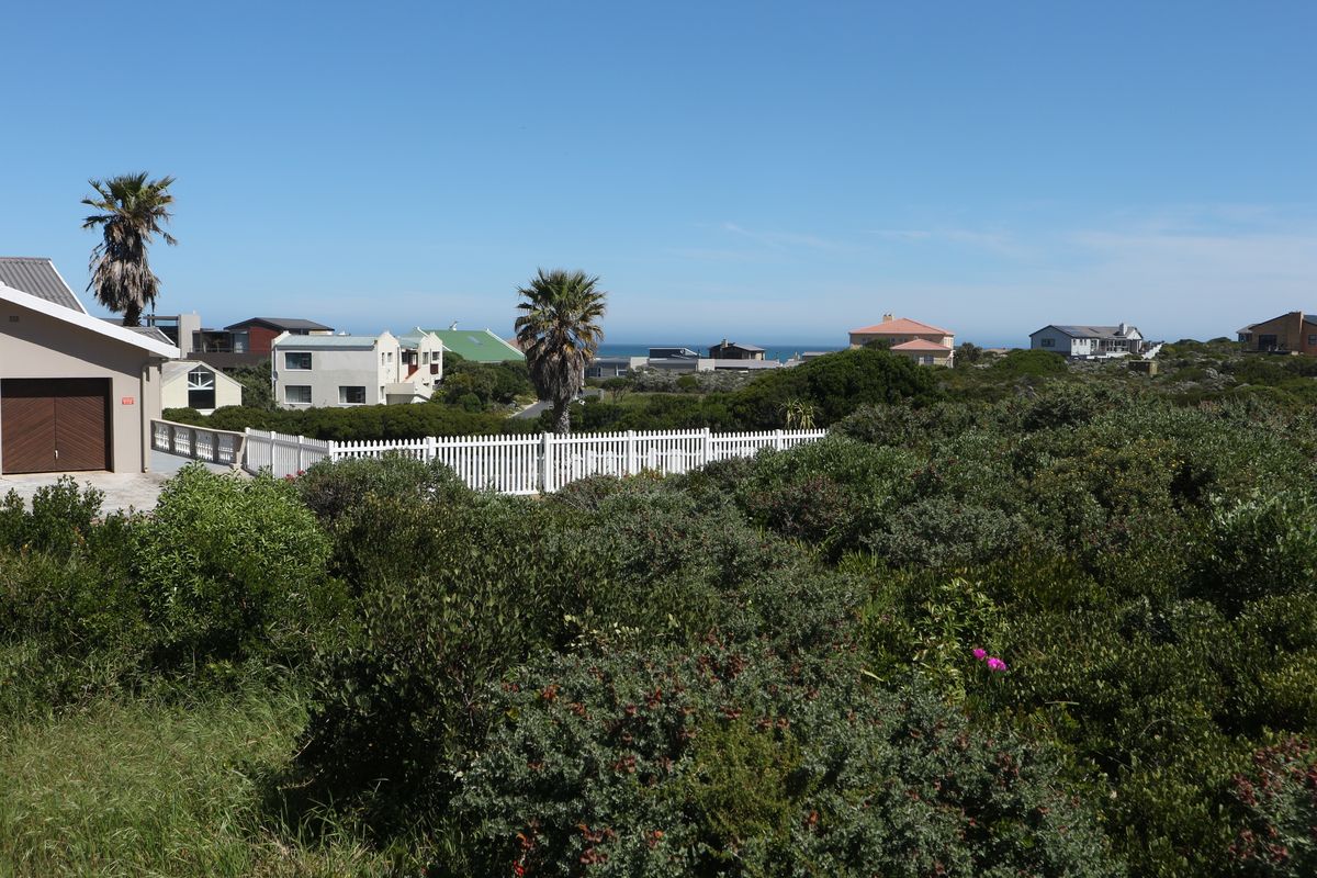 A scenic view of the surrounding residential neighborhood and coastal landscape, featuring native vegetation and a white picket fence.