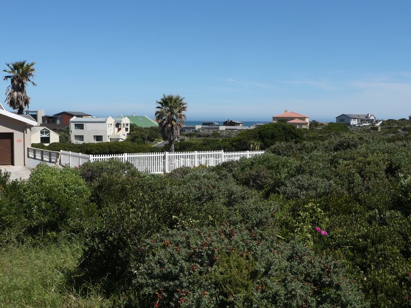 A scenic view of the surrounding residential neighborhood and coastal landscape, featuring native vegetation and a white picket fence.