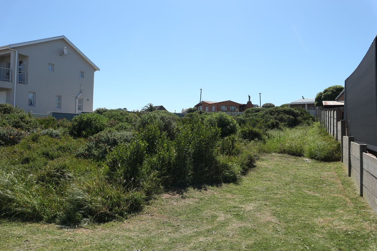A view of a vacant residential plot featuring natural vegetation, boundary fencing, and adjacent residential properties.
