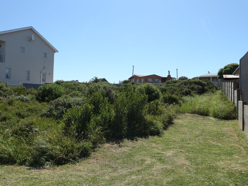 A view of a vacant residential plot featuring natural vegetation, boundary fencing, and adjacent residential properties.