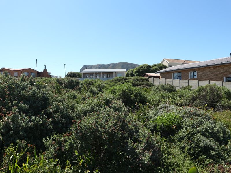 A view of a vacant residential plot featuring dense indigenous vegetation and a precast concrete boundary wall with neighboring properties in the background.