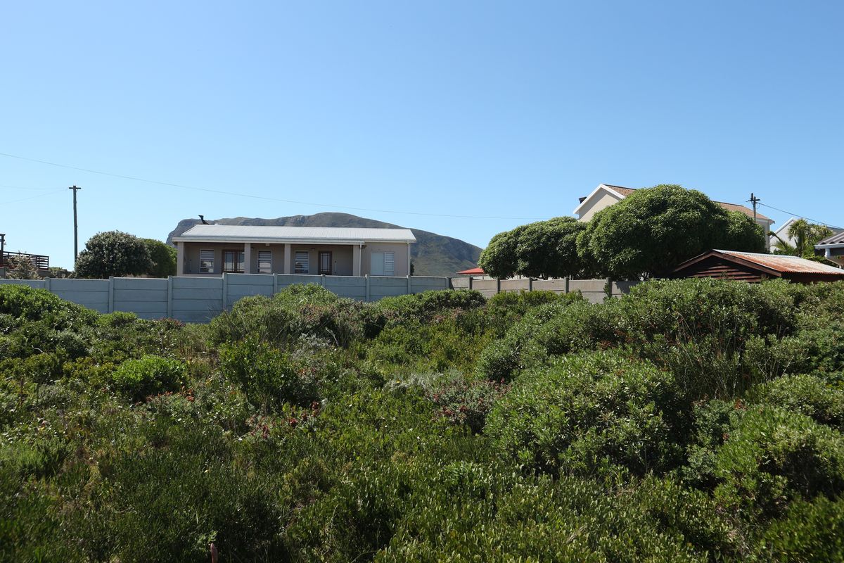 A view of a vacant residential plot featuring dense indigenous vegetation and a precast concrete boundary wall with neighbouring properties in the background.