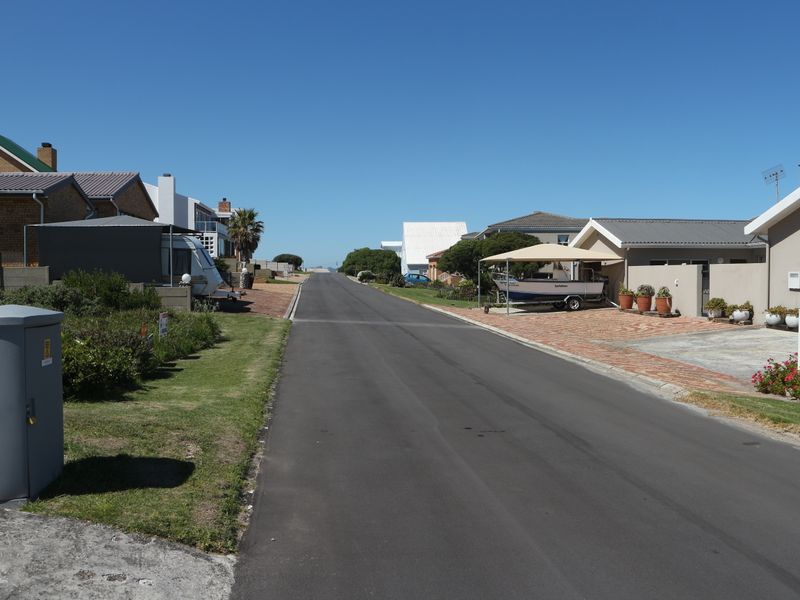 A clear street view showing the residential neighborhood approach with paved roads, driveways, and established boundary walls.