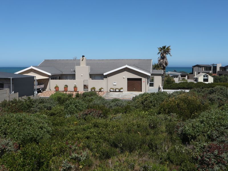 Front elevation of a residential property featuring a tiled roof, garage, and paved driveway, set within a coastal landscape.