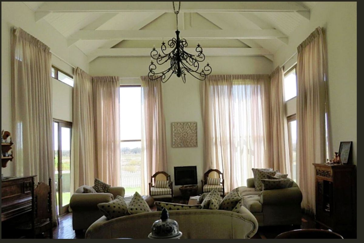 Spacious living room featuring a high vaulted ceiling with exposed trusses, a built-in fireplace, and large windows providing ample natural light.