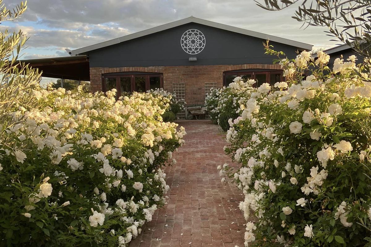 A charming rear view of the property featuring a brick pathway leading to a well-maintained building with an exposed brick facade and covered patio.