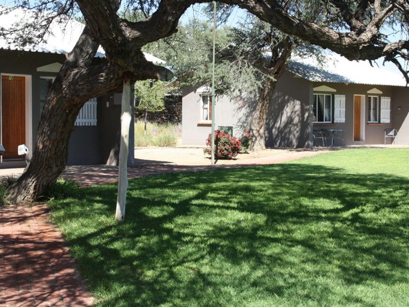 View of the rear exterior of the small holding units, featuring brick pathways, well-maintained lawn, and established trees.