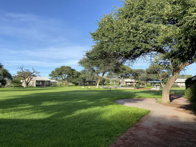 Expansive landscaped garden area featuring a paved walkway, mature trees, and multiple detached outbuildings set within a well-maintained green space.