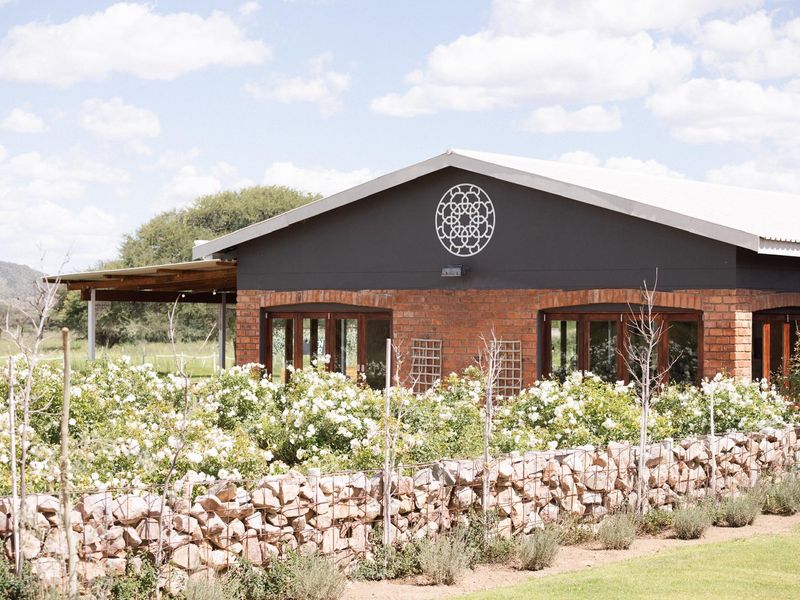 A charming brick-built structure featuring a metal roof, stone gabion garden wall, and expansive timber-framed glass doors opening onto a covered patio area.